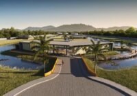 Clube moderno do Condomínio Allegro, com design angular, grandes janelas de vidro, cercado por lago e deck de madeira.