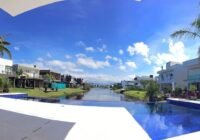Condomínio Malibu Beach Residence em Xangri-lá, RS: casas modernas, canal, piscina azul, palmeiras. Céu claro e gramados v...