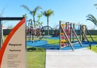 Playground moderno com piso emborrachado azul, estruturas de madeira e metal, e área verde no Condomínio Sunset Xangri-Lá.
