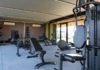 Academia do Condomínio Sunset Xangri-Lá com equipamentos de musculação e cardio pretos, piso cinza emborrachado, paredes e...
