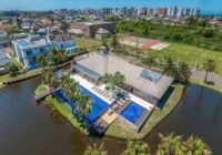 Vista aérea do clube principal do Condomínio Villaggio Atlântida, com piscinas, decks de madeira e lago sereno, em Xangri-...
