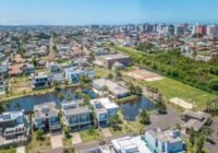 Vista aérea do Condomínio Villaggio Atlântida, com casas modernas, lago, quadras esportivas, e a cidade de Capão da Canoa ...